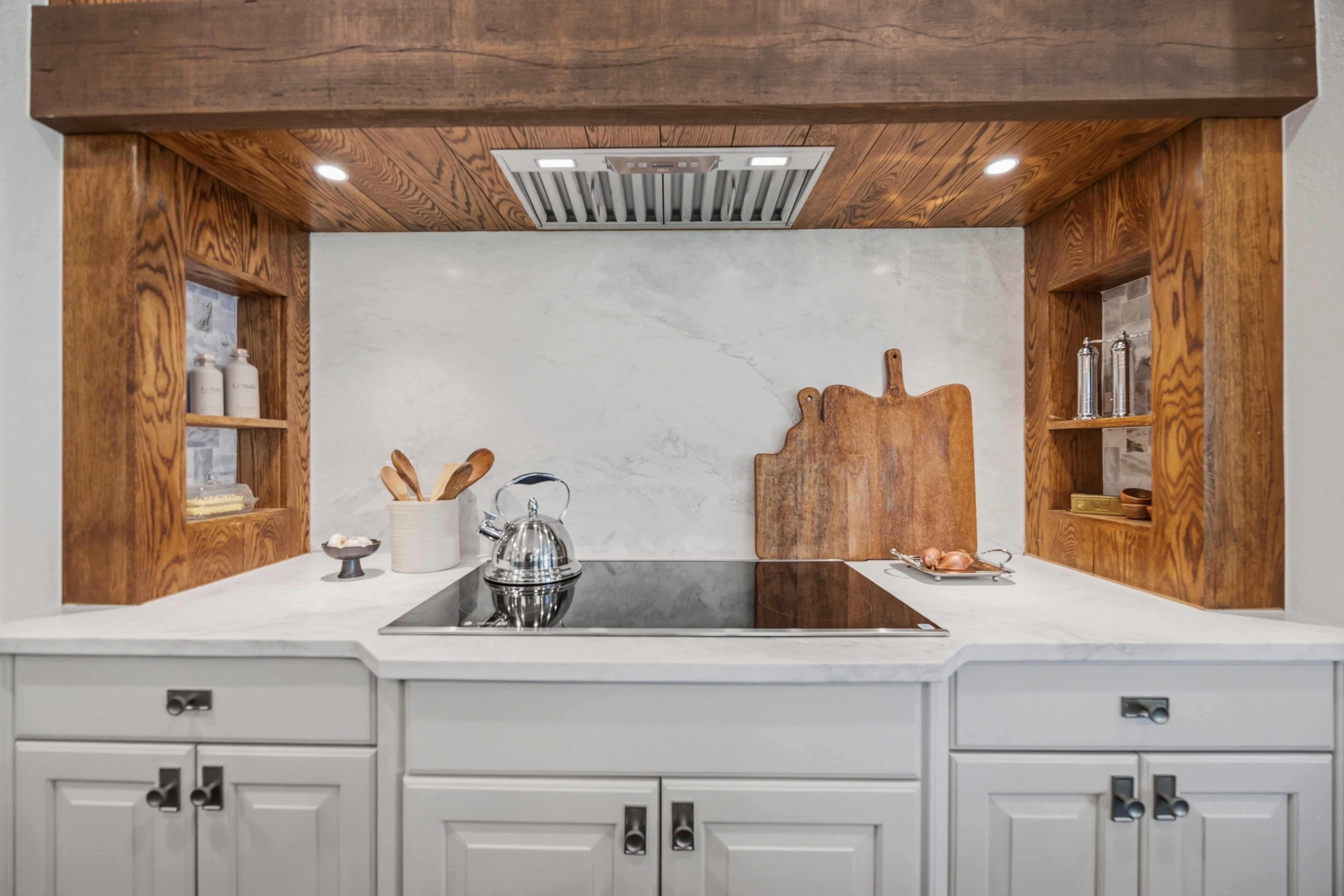 Custom kitchen range alcove with rich wood paneling, marble backsplash, white cabinetry, and built-in shelving in a Greenwood Village, CO kitchen remodel