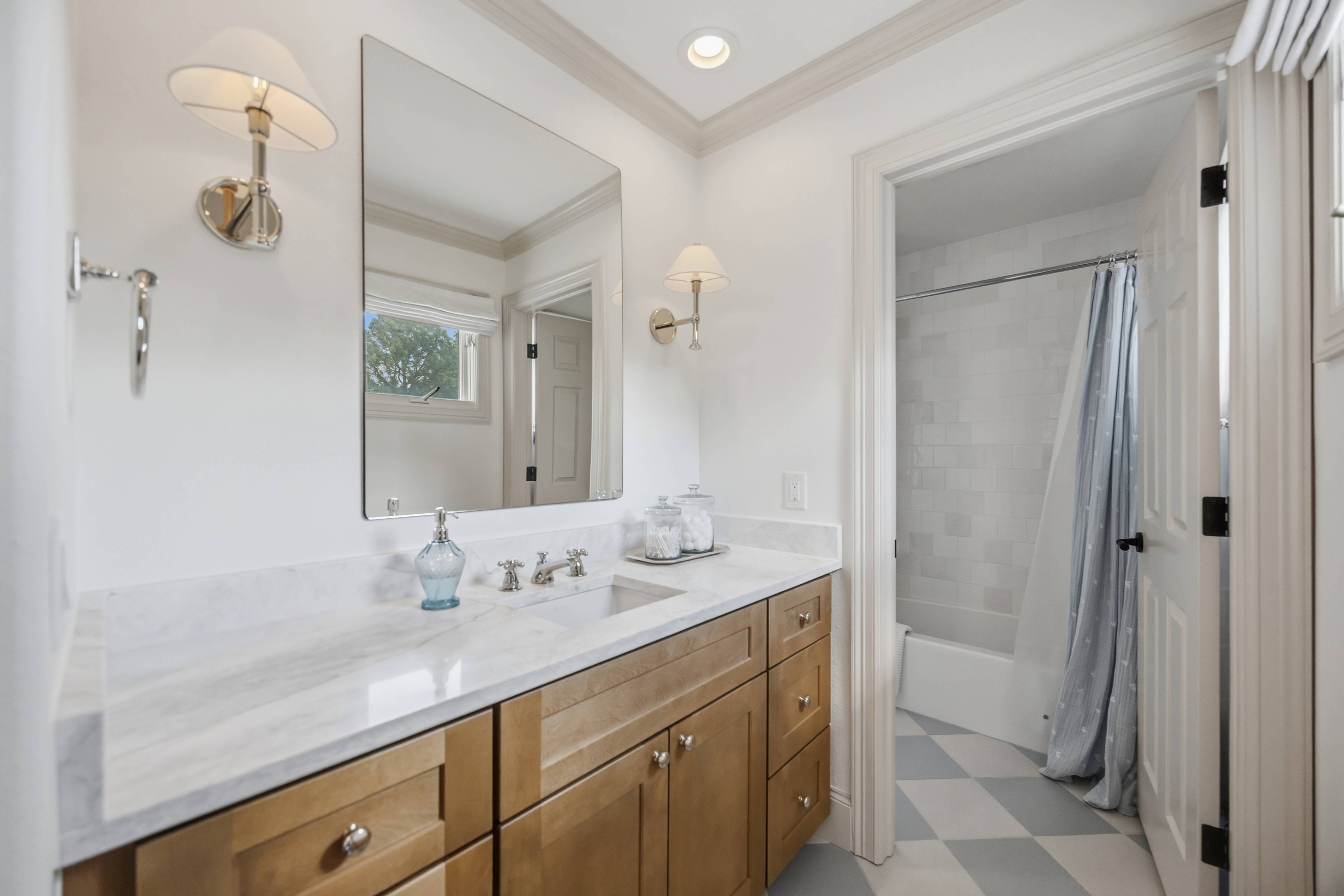 Remodeled guest bathroom featuring a natural wood vanity, marble countertop, polished fixtures, and a white tiled shower in Greenwood Village, CO