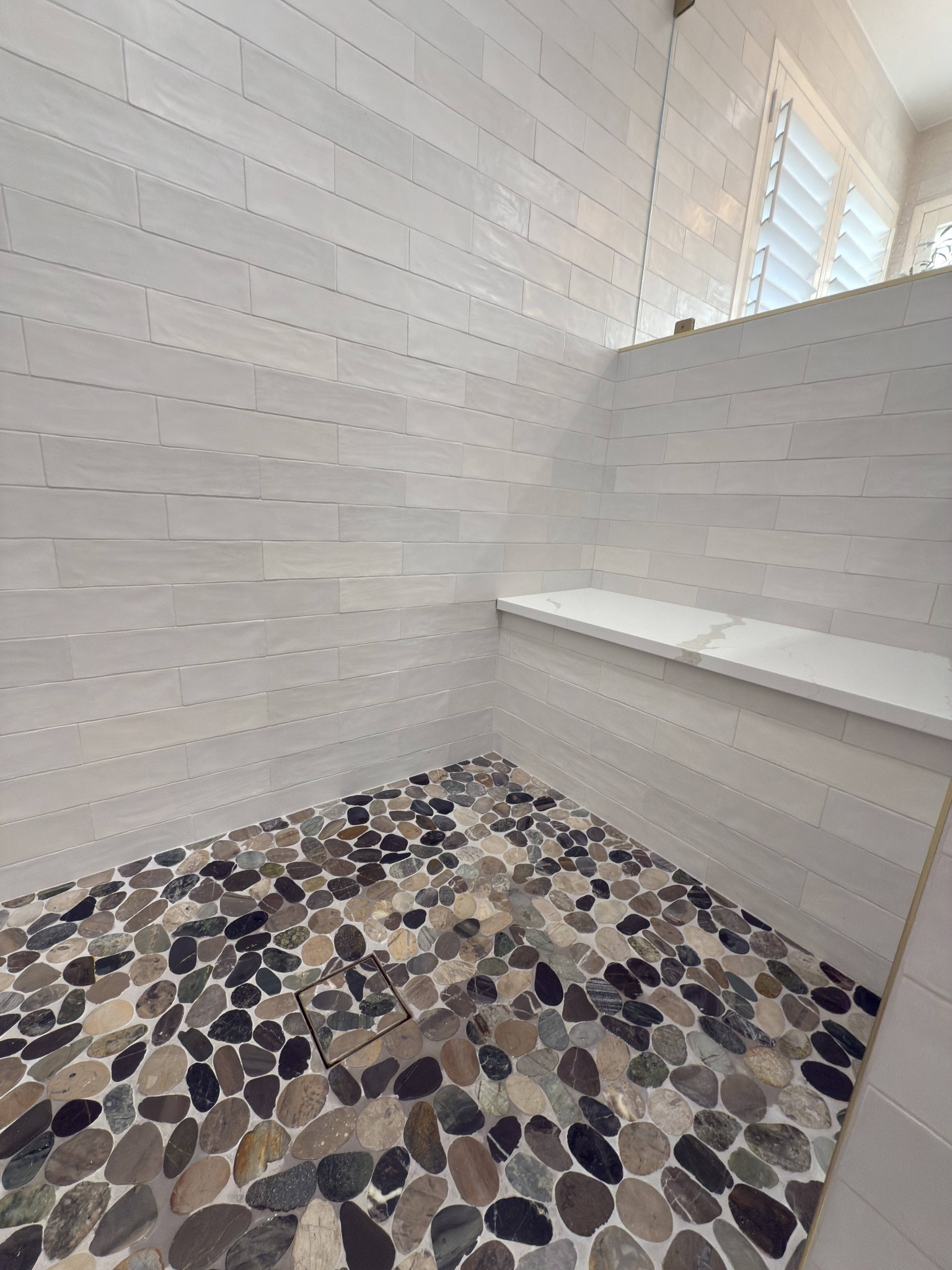 after littleton bathroom remodel pebble shower floor with white wall tile and quartz ledge