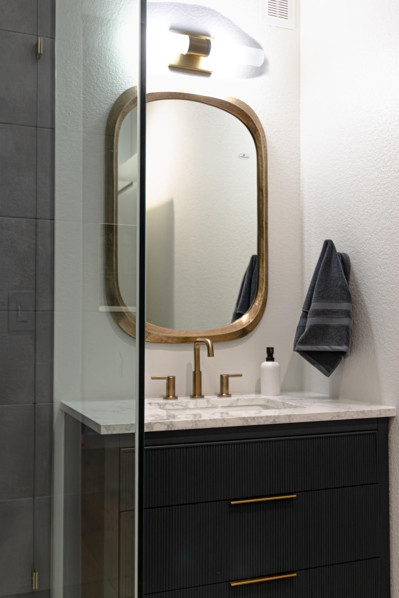 Gold mirror and black vanity with white granite countertop in bathroom in basement remodel in Denver